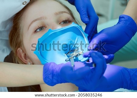 Fastening a special metal clamp to the patient's tooth with a clasp to hold it on the tooth Cofferdam or latex curtain. close-up. the dentist's hands in the frame