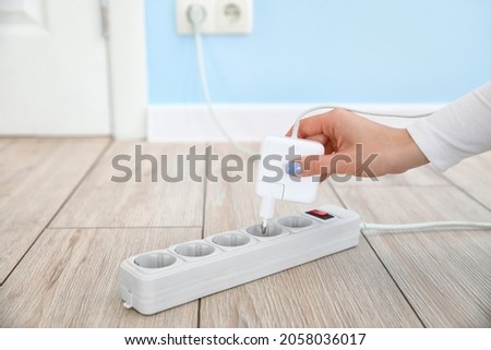 Woman inserting plug into extension cord in room Royalty-Free Stock Photo #2058036017