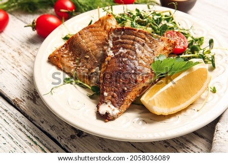 Plate with tasty baked cod fillet and vegetables on light wooden background, closeup