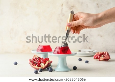 Woman eating tasty berry jelly on light background Royalty-Free Stock Photo #2058045056