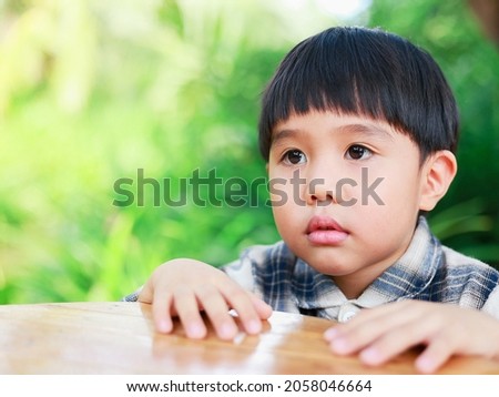 one boy wearing a retro shirt Which sits in the outdoor garden with a wooden table with a nervous embarrassed mood with a blurry bokeh background and copy space on a sunny day