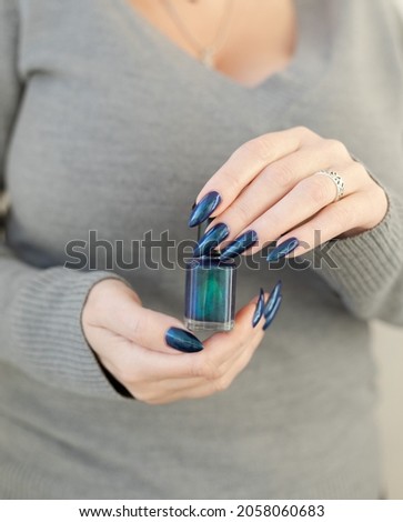 Woman hand with long nails and turquoise blue green manicure with bottles of nail polish