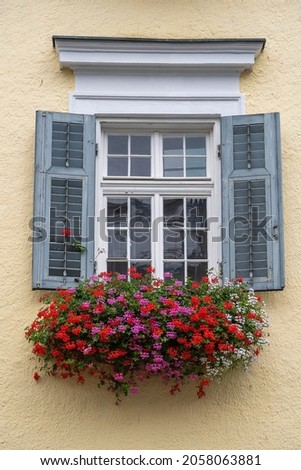 Beige plaster facade of a mountain house and windows with colorful flowers in Austria, close up