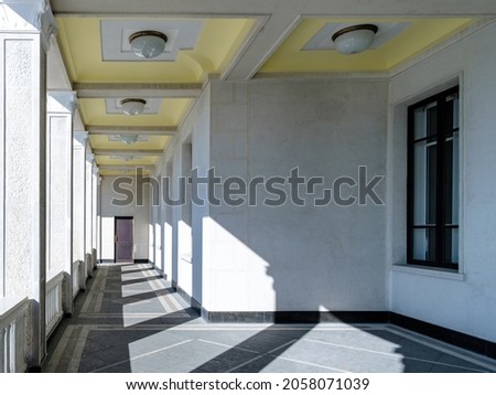 View of the columns in the gallery in an unknown building. Bright sunlight through the columns creates a geometric pattern of light and shadow on the floor and walls.