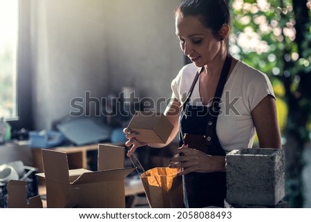 Craftswoman working in her workshop packing decorative concrete vase for shipping.