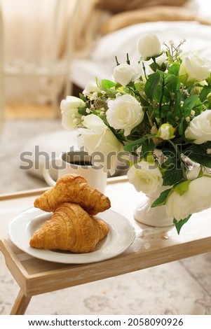 Coffee and croissant on a wooden tray for breakfast, good mood, sunny morning, breakfast in bed, interior in an apartment or in a hotel