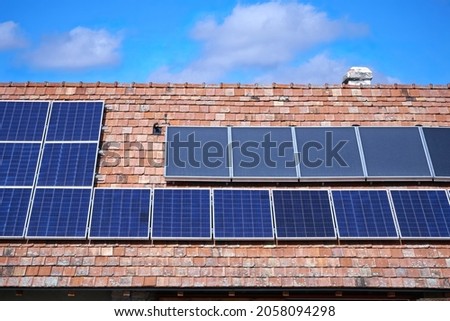 Solar panels (which converts sunlight into electricity) and solar collectors (which heats water by sun) on a classic tiled roof. Color illustration photo of clean, renewable energy sources.