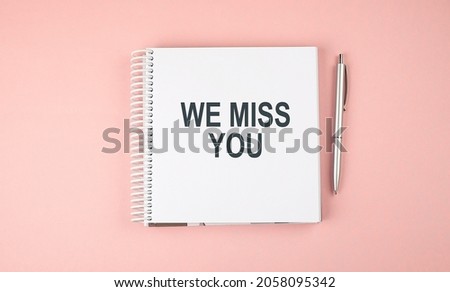 WE MISS YOU text on notebook with pen on pink background