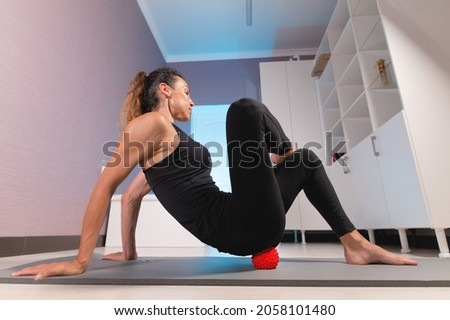 Close-up young caucasian woman doing myofascial self-massage of her thigh and buttocks with a massage ball on a massage mat. 4k resolution