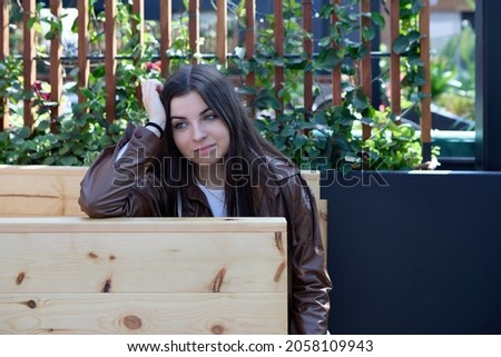 smiling young woman sitting on a terrace outside pensive