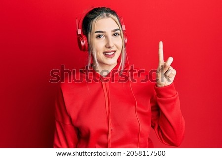 Young modern girl wearing gym clothes and using headphones showing and pointing up with finger number one while smiling confident and happy. 