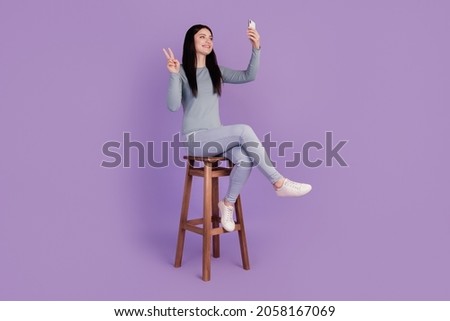 Full size profile side photo of young girl sit stool make selfie show peace v-symbol isolated over purple color background