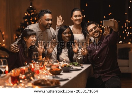 holidays, party and celebration concept - multiethnic group of happy friends having christmas dinner at home and taking selfie with smartphone