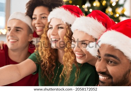 winter holidays and people concept - happy friends in santa hats taking selfie at christmas party over christmas tree lights background