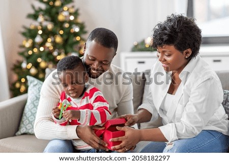 family, winter holidays and people concept - happy african american mother, father and baby son opening gift box with toy at home on christmas