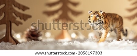 Figurine of tiger, wooden fir trees in snow on beige background. Tiger symbol of the Chinese new year 2022. Christmas greeting card. Banner