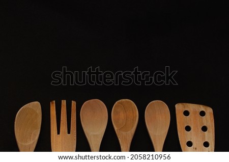 Six wooden cooking utensils isolated on black background with copy space