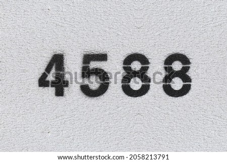 Black Number 4588 on the white wall. Spray paint. Number four thousand five hundred and eighty.