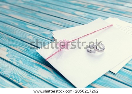 Envelope decorated with pink flower and two wedding rings on blue background