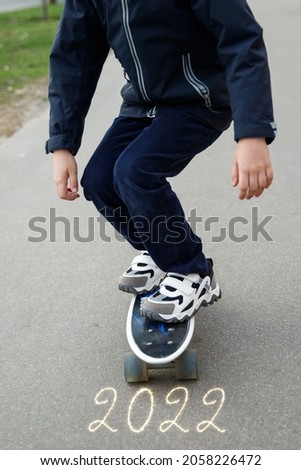 Children's feet in white sneakers and blue trousers on a skateboard, nra asphalt inscription 2022.