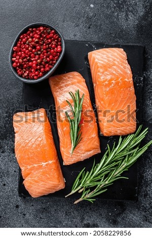 Raw salmon fillet steaks on marble board with herbs. Black background. Top view