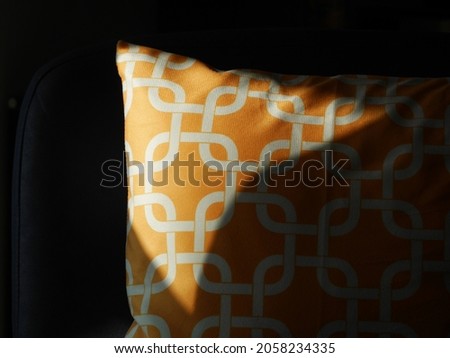 A yellow throw pillow cushion with white geometric patterns in dramatic lighting