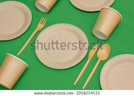 Recyclable fork, spoon, knife, plate and cup on a green background. Kitchen utensils are served on the table. Top view. Minimalist Style. Copy space.