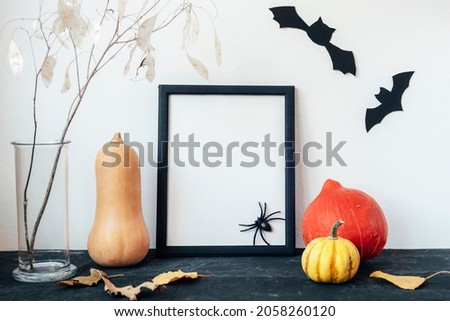 Blank picture frame, hokkaido pumpkins, lunaria dry flowers in glass vase, bats and spider on black table. Mockup, copy space. Halloween holiday concept.