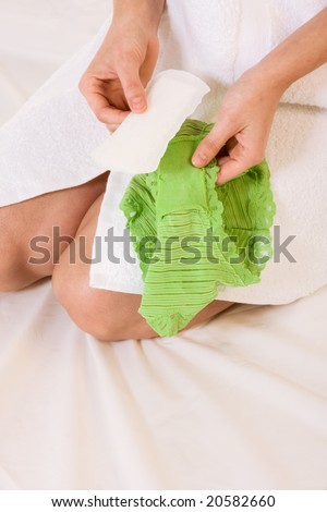 Close up of female hands holding feminine hygienic pad, preparing to stick it to her green panties