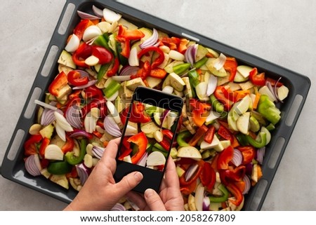 An adult woman takes pictures of stewed vegetables on the phone for social networks or a culinary blog, top view, home cooking hobby, healthy lifestyle