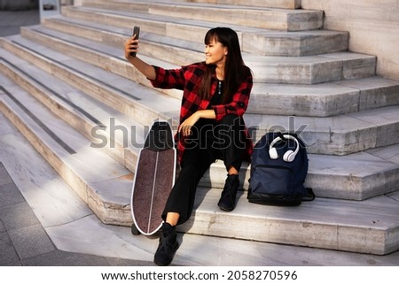Portrait of beautiful girl with skateboard. Happy smiling woman taking selfie photo.	