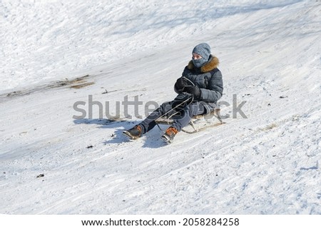 The guy goes down on a sled on a slippery snow slide.