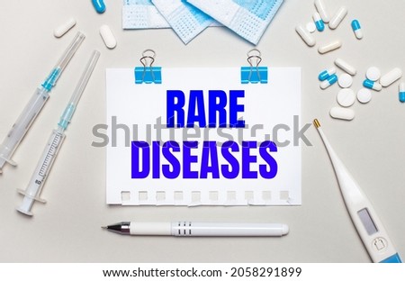 On a light gray background, blue medical masks, syringes, an electronic thermometer, pills, a pen and a notebook with the inscription RARE DISEASES . Medical concept