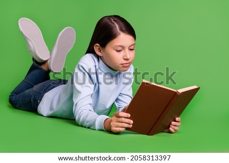 Photo of shiny serious school girl dressed blue turtleneck lying floor reading book isolated green color background