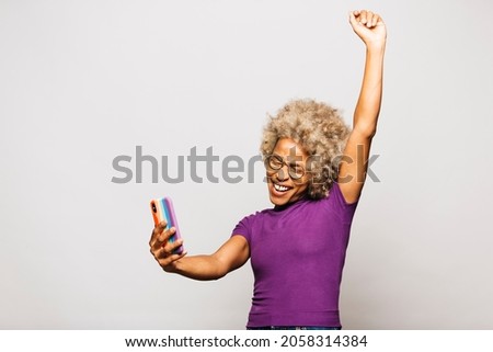 Portrait of Smiling Young woman using smart phone with a rainbow flag case while standing Against White Background