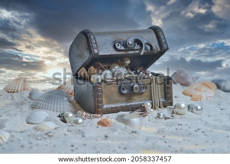 old Wooden treasure chest filled with treasures on sand on the beach with dramatic blue sky