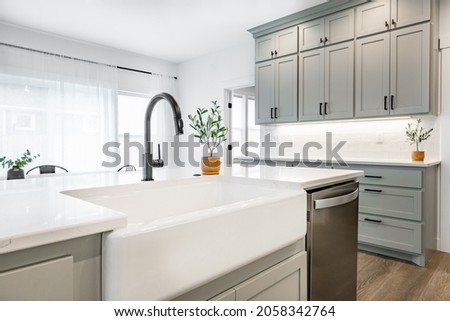 modern farmhouse style kitchen with stainless appliances white counter top raw wood dining table kitchen island and mirror reflection Royalty-Free Stock Photo #2058342764