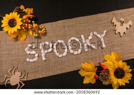 Spooky written with white stones over a burlap banner with yellow flowers and black background