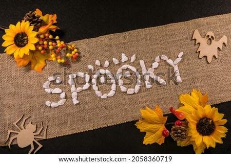 Spooky written with white stones over a burlap banner with yellow flowers and black background