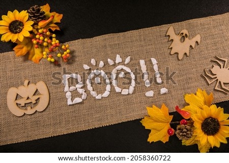 Boo written with white stones over a burlap banner with yellow flowers and black background