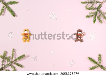 Social distance. Two gingerbread men white and black in medical masks are on a pink background with branches of a Christmas tree and white snowflakes. Minimal Christmas composition. Minimal flat lay.
