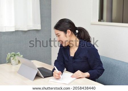 A young Asian woman takes a memo using a pen during telework at home with smile