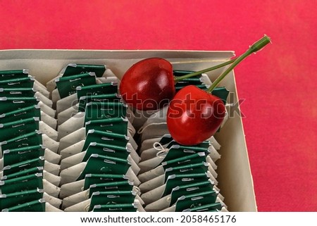 Two artificial cherries in a box with green tea bags on a red background close-up