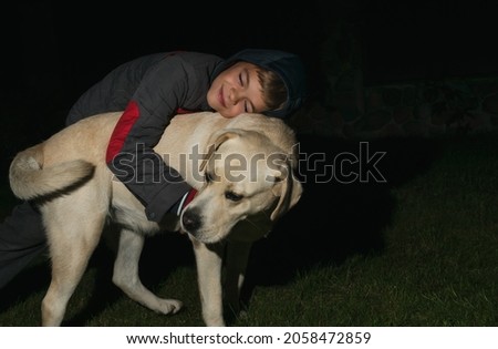 A little boy plays with a light labrador dog in the evening