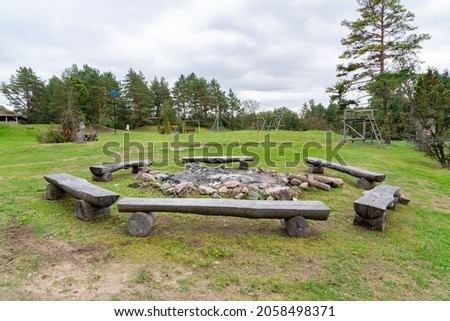 Old gathering spot around the fire pit. Wooden seats around the unlit fire pit. Green grass, early autumn, cloudy day. Circle around the fire. Campfire location. 