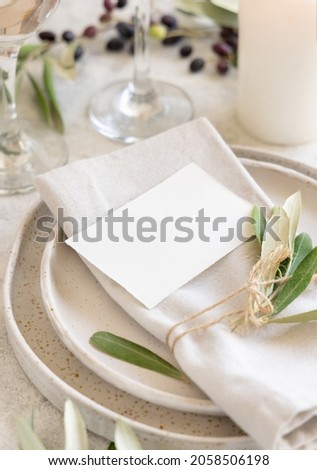 Wedding Table place with a place card and porcelain plates decorated with olive branches close up. Elegant modern template with horizontal blank paper card. Mediterranean flat lay mockup, copy space