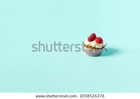 Homemade sweet cupcake with white cream and raspberries on a blue background. Sweet cake-cupcake on a colored background is a place for text.