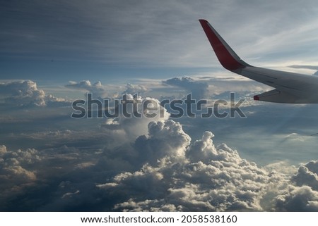 wing of airplane in sky above  clouds background of blue sky white and grey puffy clouds sky scape airplane wing in top left corner of horizontal format leaving space for type for travel vacation  Royalty-Free Stock Photo #2058538160