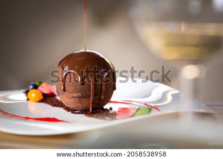 Chocolate sphere cake poured with hot chocolate on white plate in restaurant Royalty-Free Stock Photo #2058538958