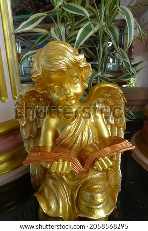 A picture of a spinning child and golden wings sitting and reading a brown book.